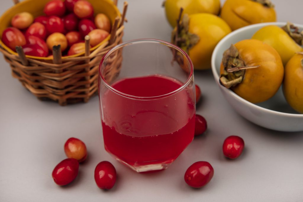 Szklanka czerwonego soku likopenowego obok świeżych pomidorów i owoców, naturalne źródło likopenu