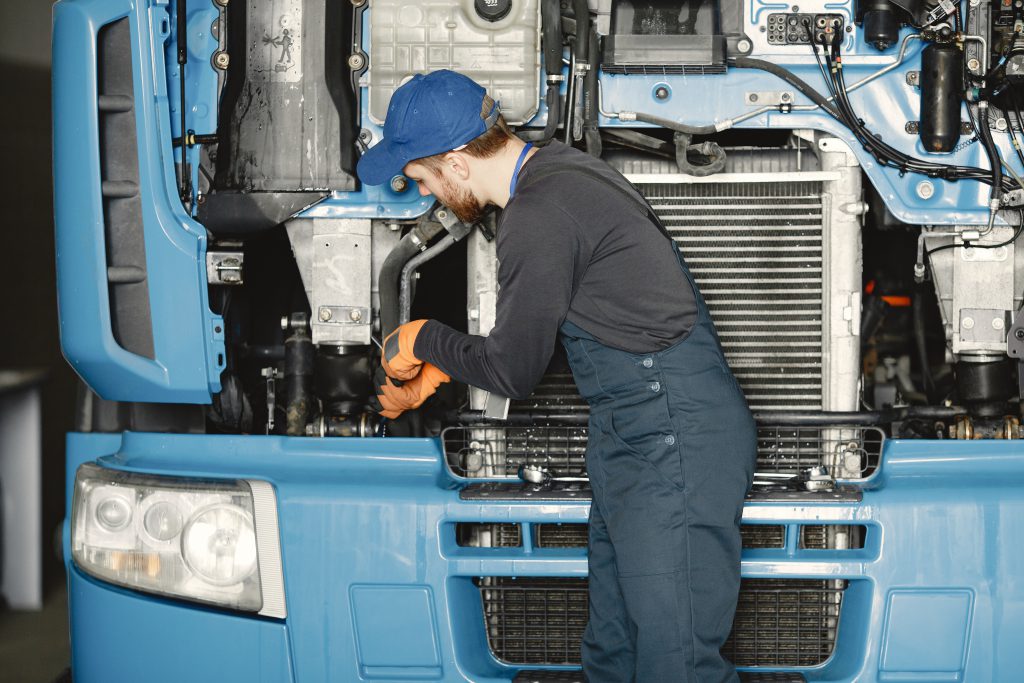 Mechanik naprawiający części samochodów ciężarowych Mercedes, wykonujący konserwację silnika i innych elementów w warsztacie samochodowym.